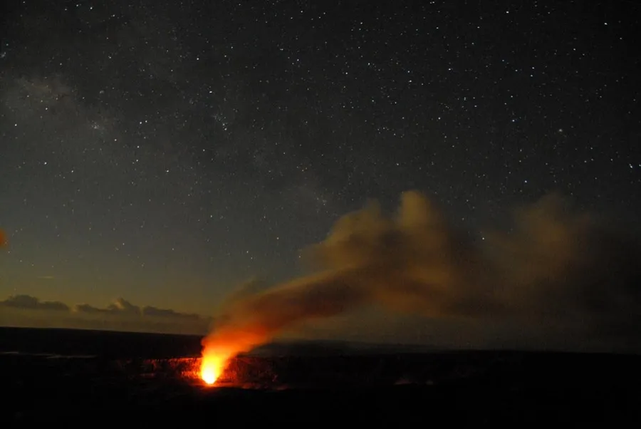 Deep orange glow from molten lava lake within Halemaʻumaʻu crater illuminating the underside of the volcanic plume at night